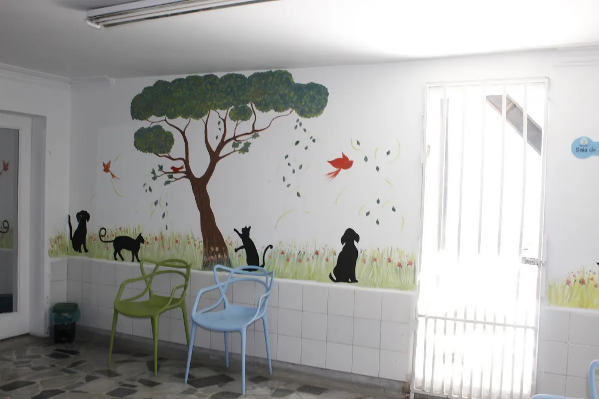 Sala de Artemisa con un mural de un árbol, perros y gatos, y sillas de colores